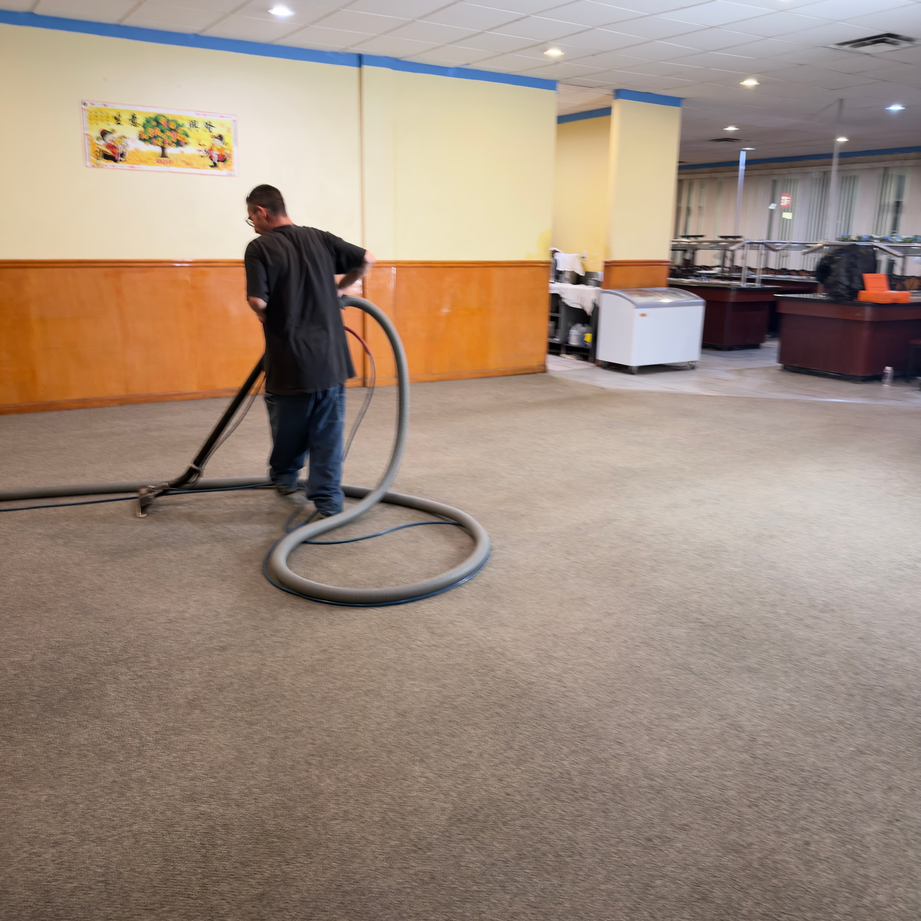 Man using professional equipment to clean the carpet in a large restaurant dining room.