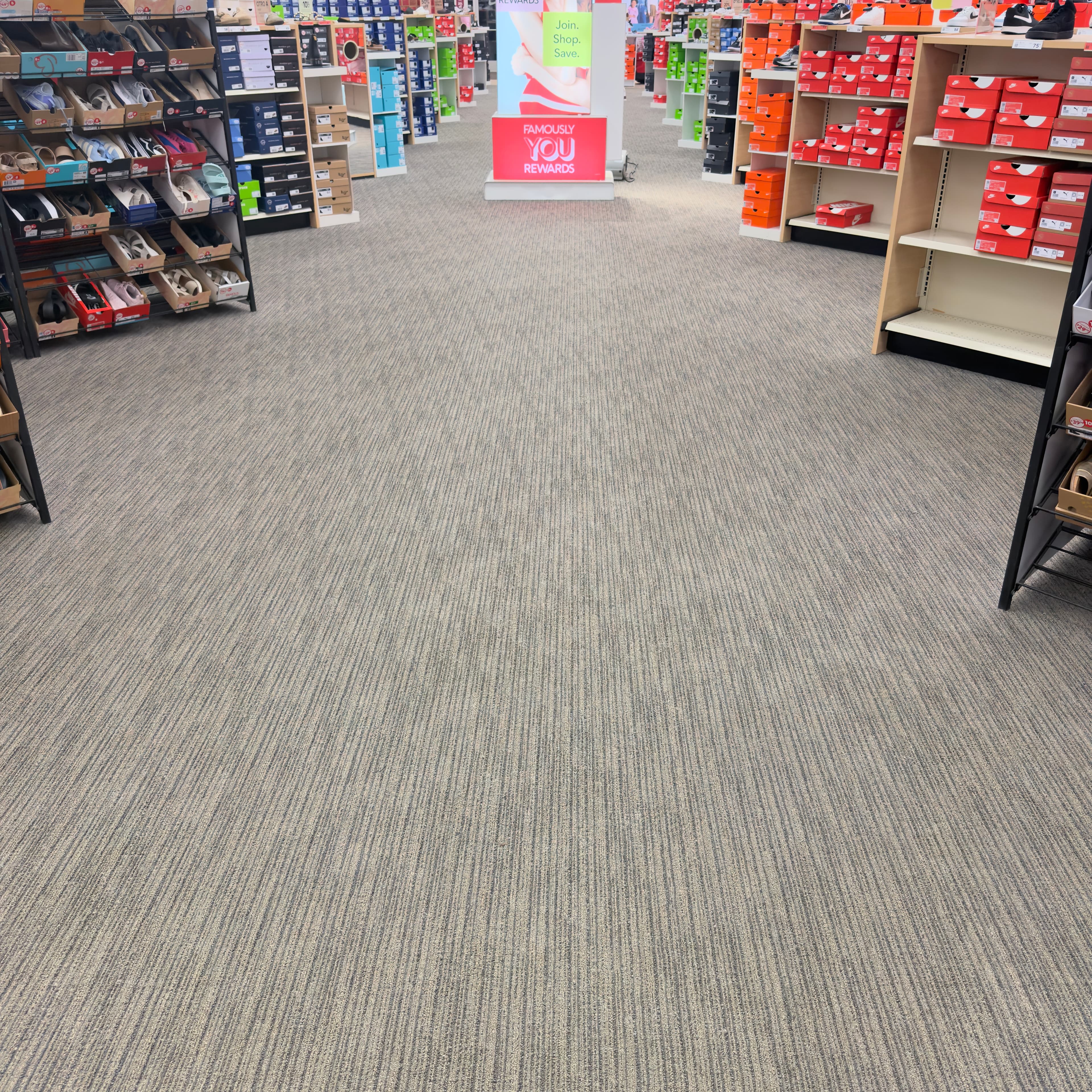 Grey carpeted aisle in a shoe store lined with shelves of shoes and boxes.