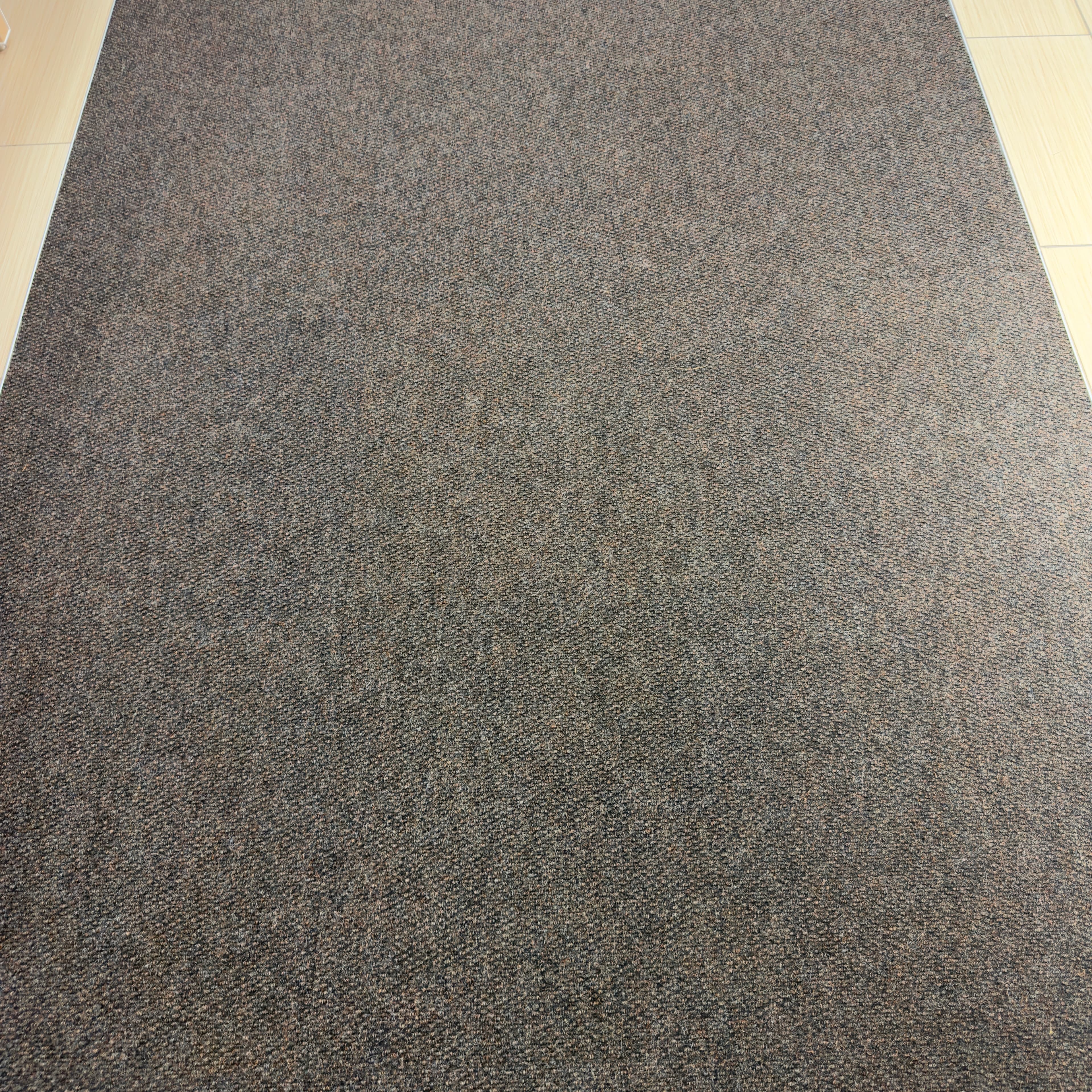 Large dark grey textured floor mat runner laid on top of light-colored wood-look flooring.
