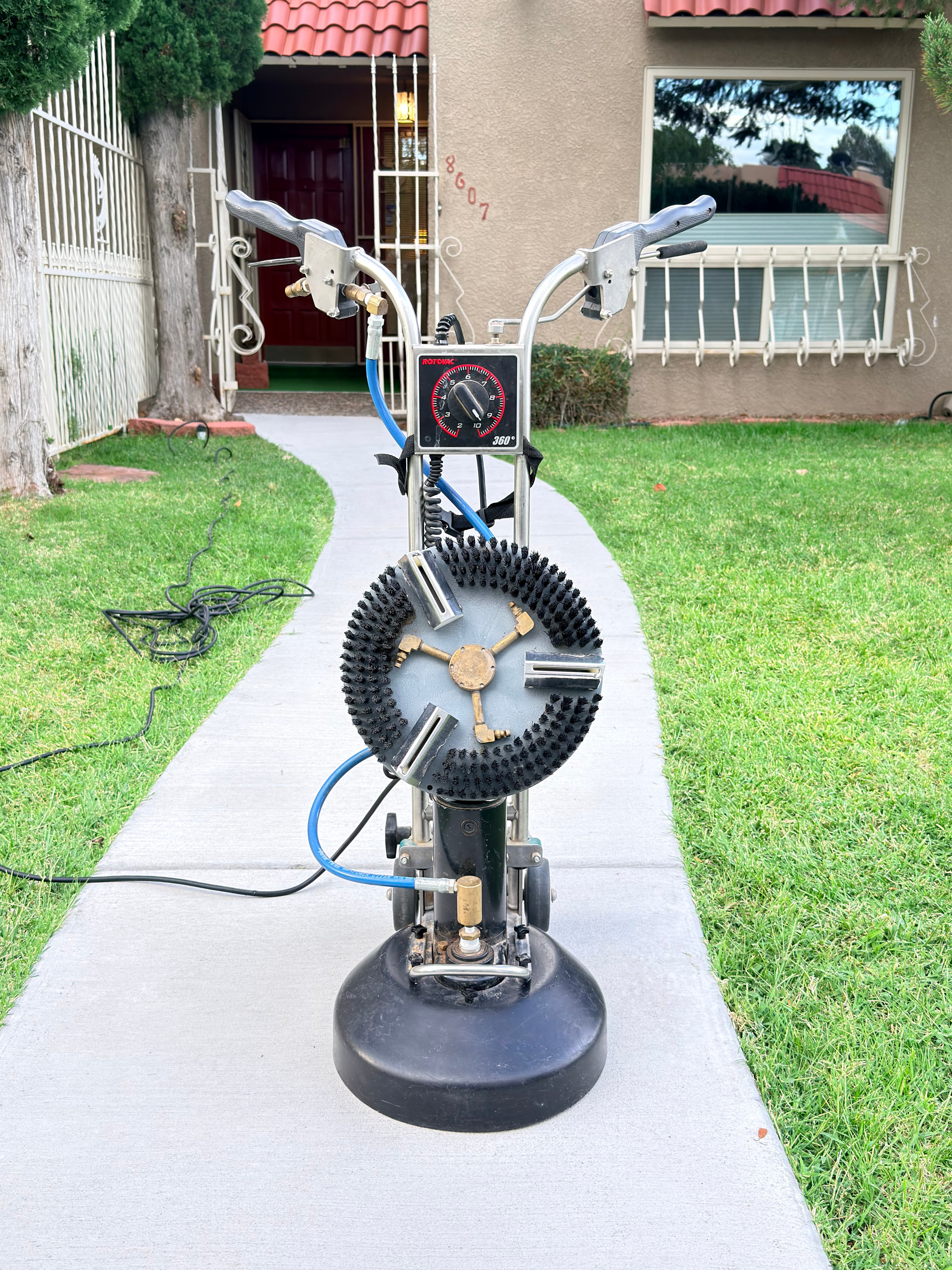 Rotovac carpet cleaning machine with circular brush head on a concrete walkway outside a house.